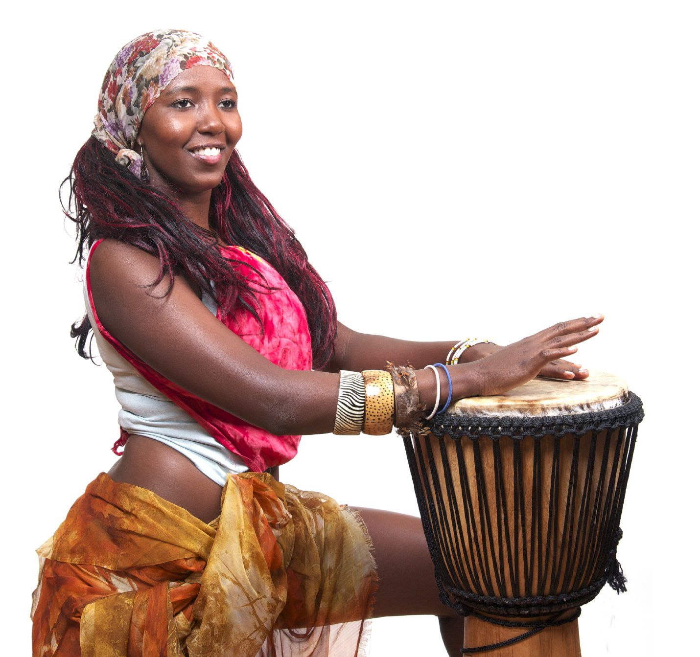 Smiling Black woman in colorful outfit, playing a single drum.