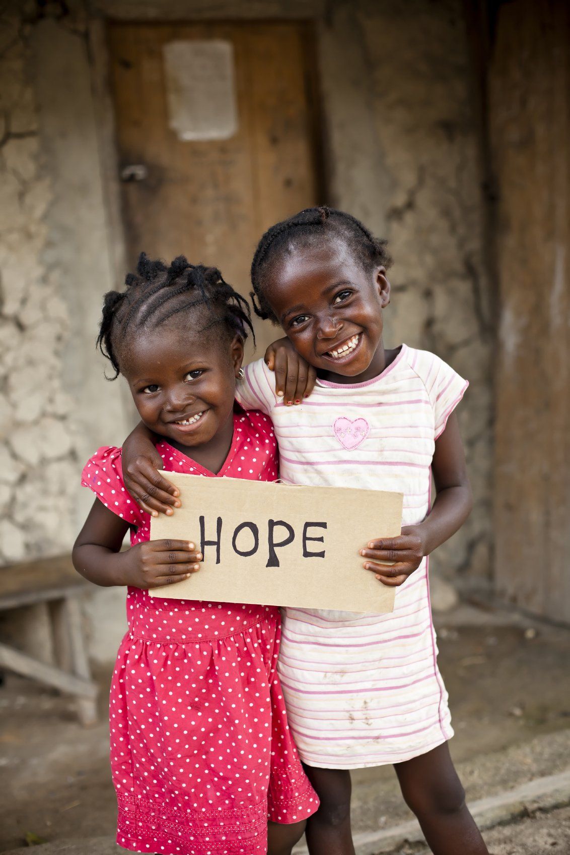 Two, little African girls, hugging each other and holding a 