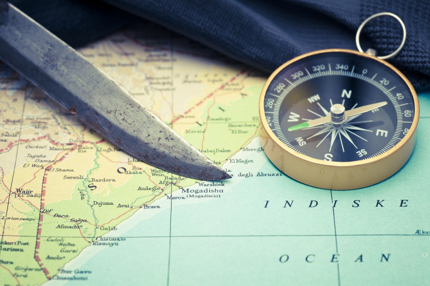 A photo of a knife blade and a small gold compass, sitting on a map of the world.