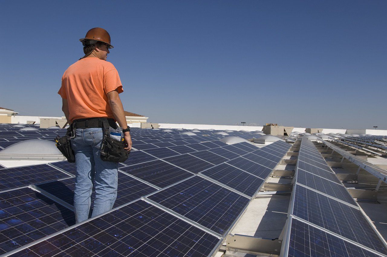 A solar energy technician, in orange t-shirt, walking among an array of ground-based solar cells.