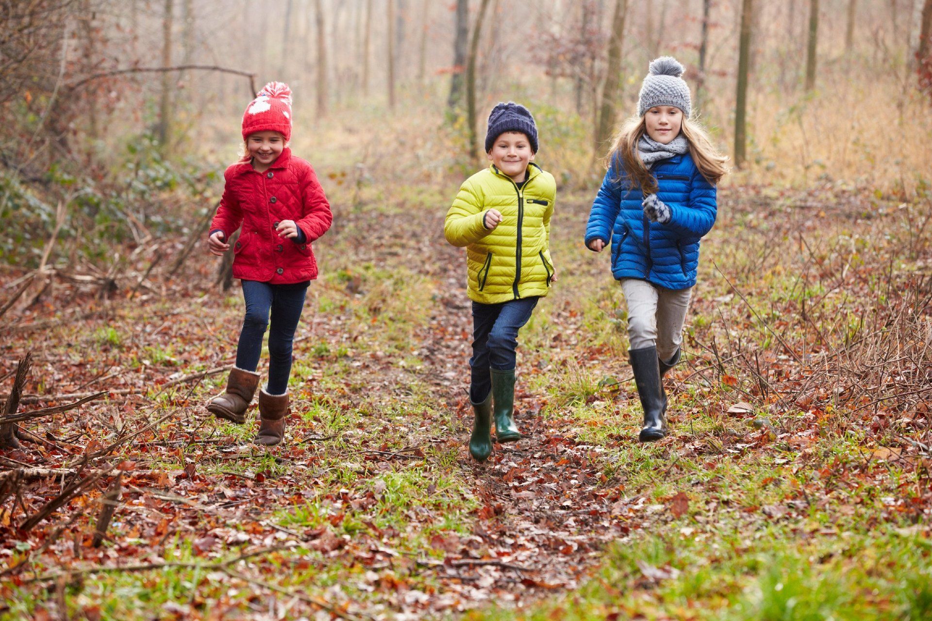 Three young siblings in colorful clothing, running through the woods