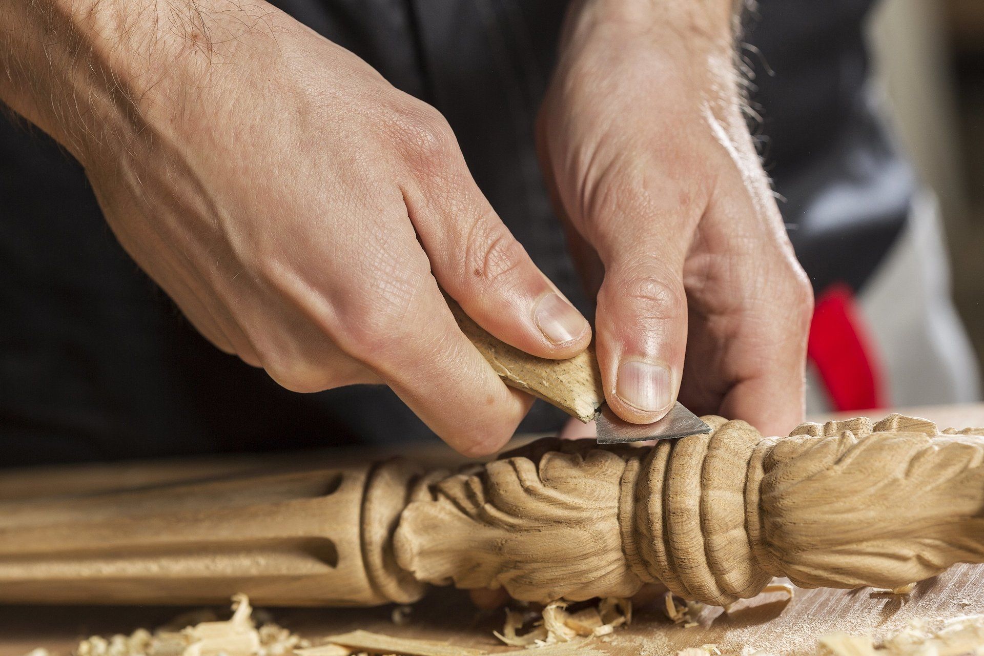 Two hands of a woodworker sculpting a piece of wood