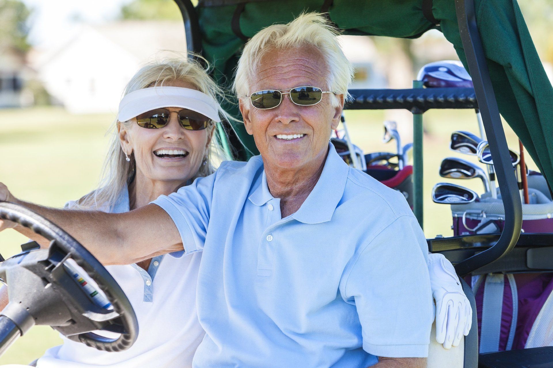 A retired husband and wife riding in a golf cart, at the golf club.