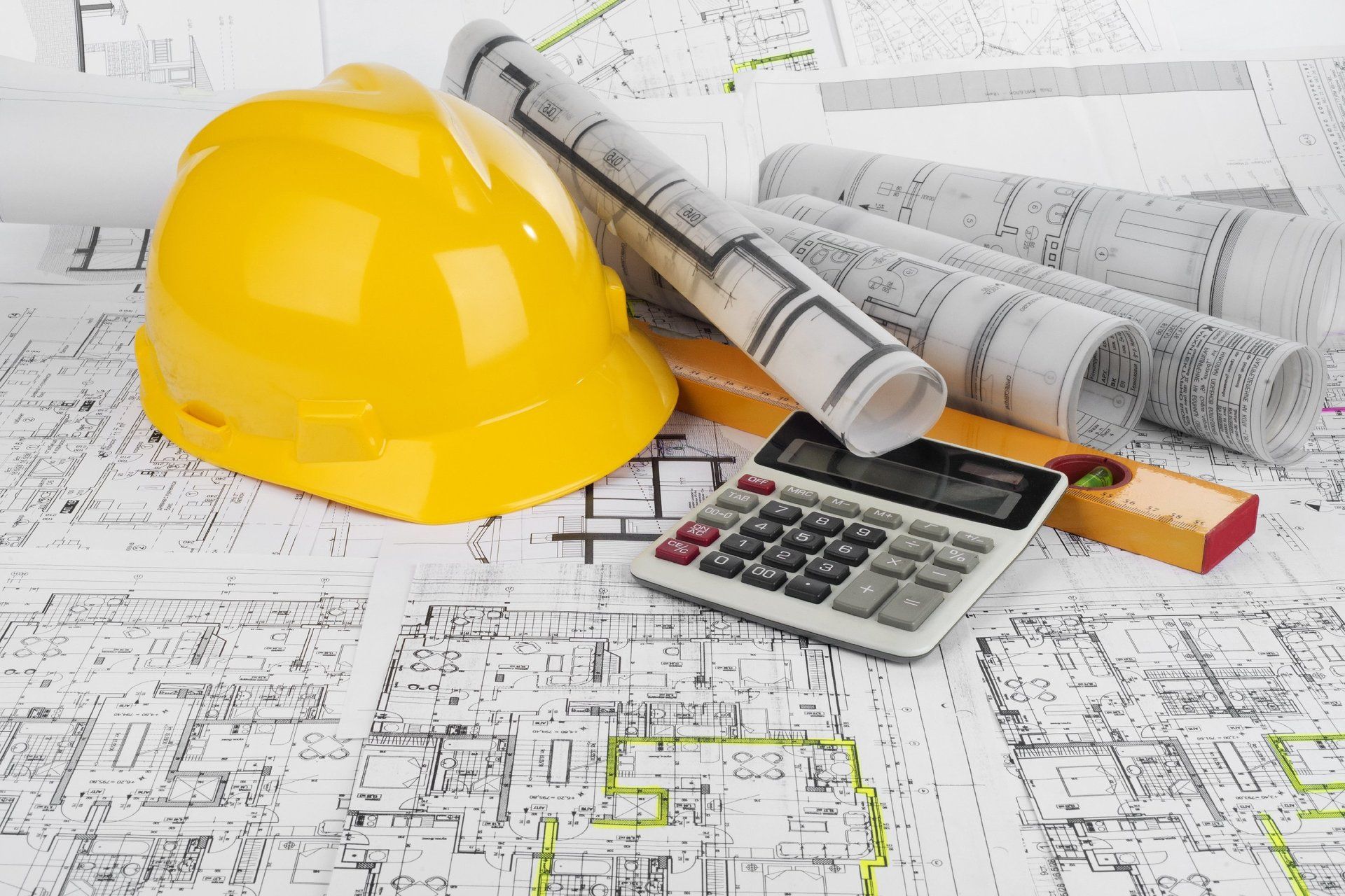 A yellow hard hat, calculator and a set of architectural plans sitting on a table.
