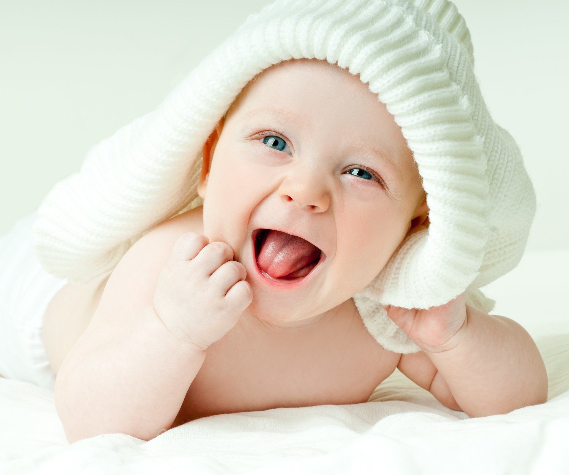 Image of a white baby, laying on its stomach with head up, smiling, with tongue out.