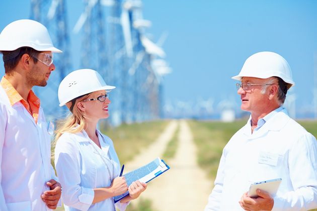 Das Bild zeigt eine Ingenieurin und zwei Ingenieure im Gespräch vor Windkrafträdern