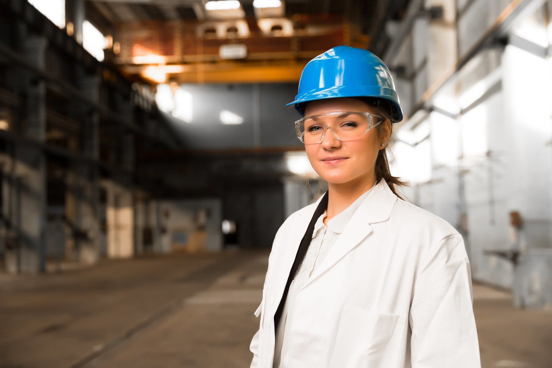 A female engineer, wearing a blue hard hat, standing in front of the factory.