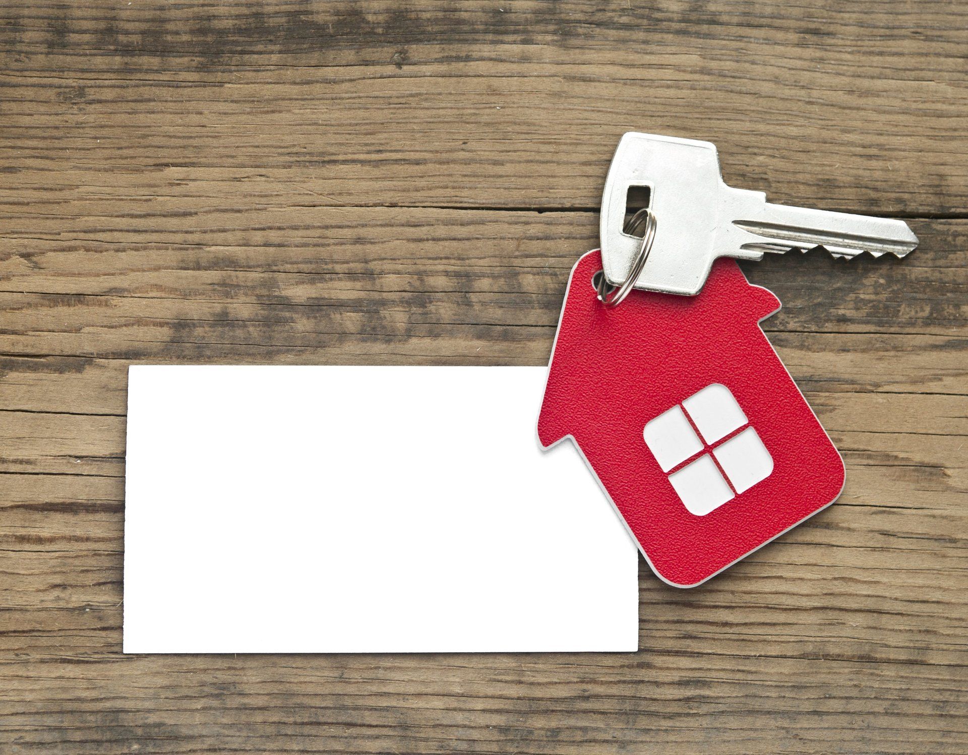 Hausförmiger Schlüsselanhänger einer Immobilie mit Rent-to-buy Option in Italien, mit Schlüssel und leerer weißer Karte auf Holzhintergrund.