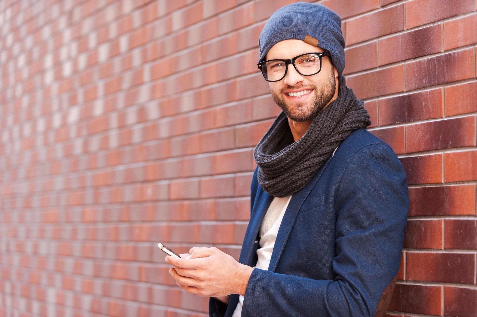 Man holding mobile phone leaning against brick wall
