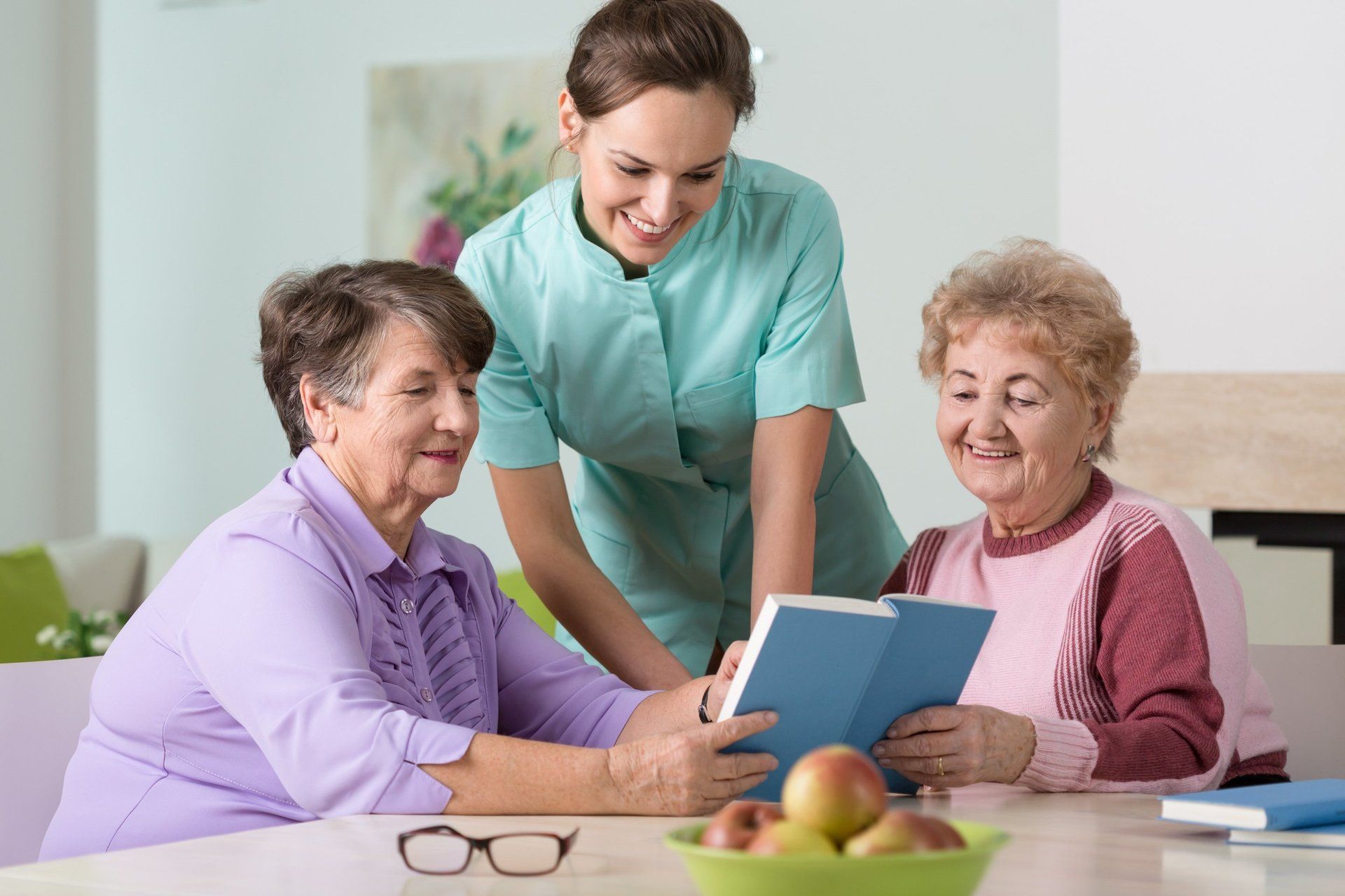 Two senior citizens and a nurse discussing a book.