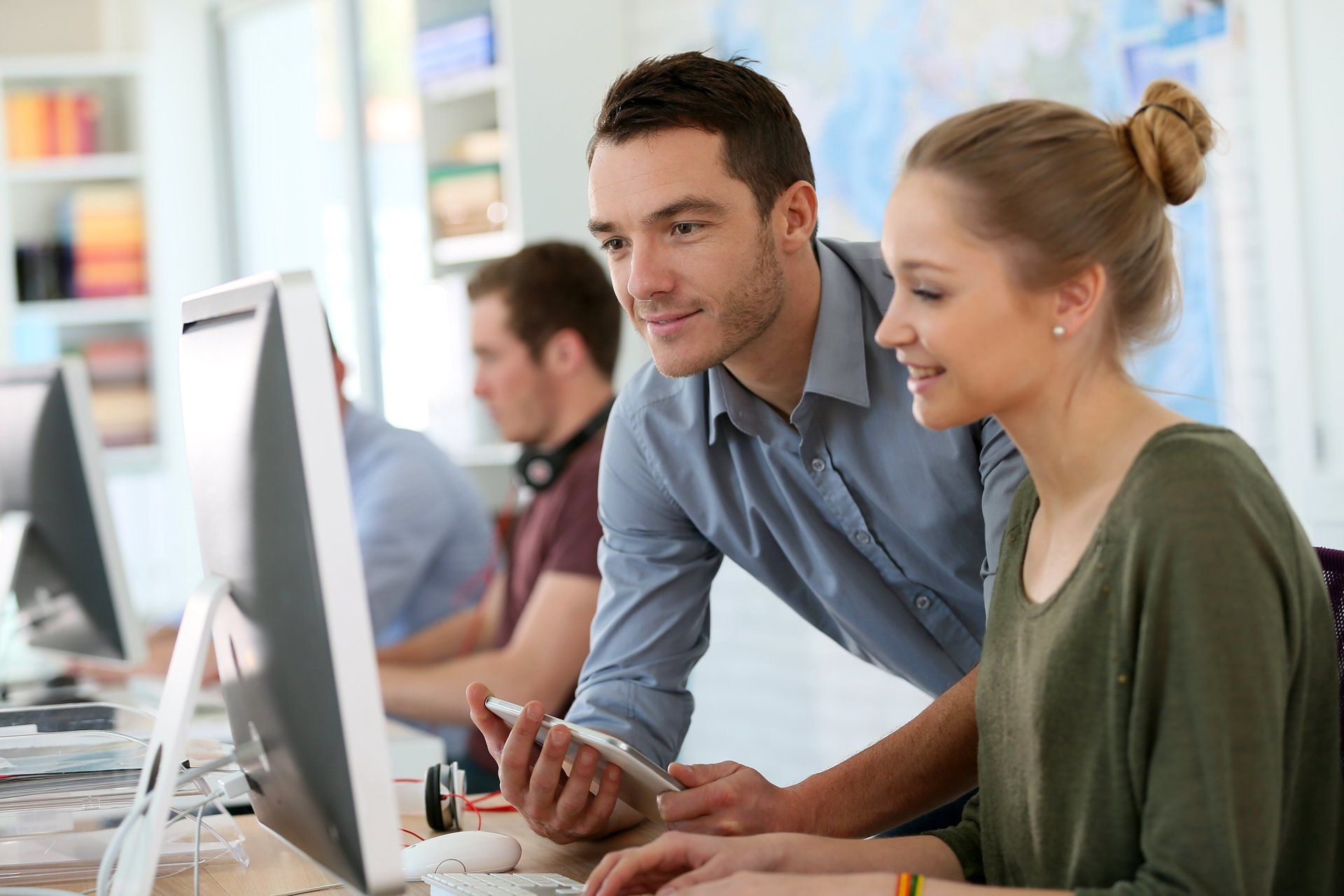 Man in grey shirt working at desktop computer  and woman green sitting at same computer