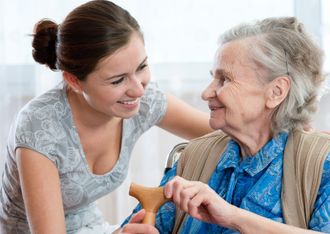 Image shows an elderly lady and a carer with her arm around her both are smiling