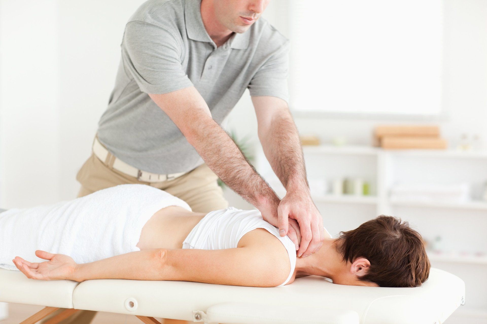 Massage guy. Фото работы мануального терапевта. Делает массаж девушке папы. Мужчина лежит на спине во время массажа.