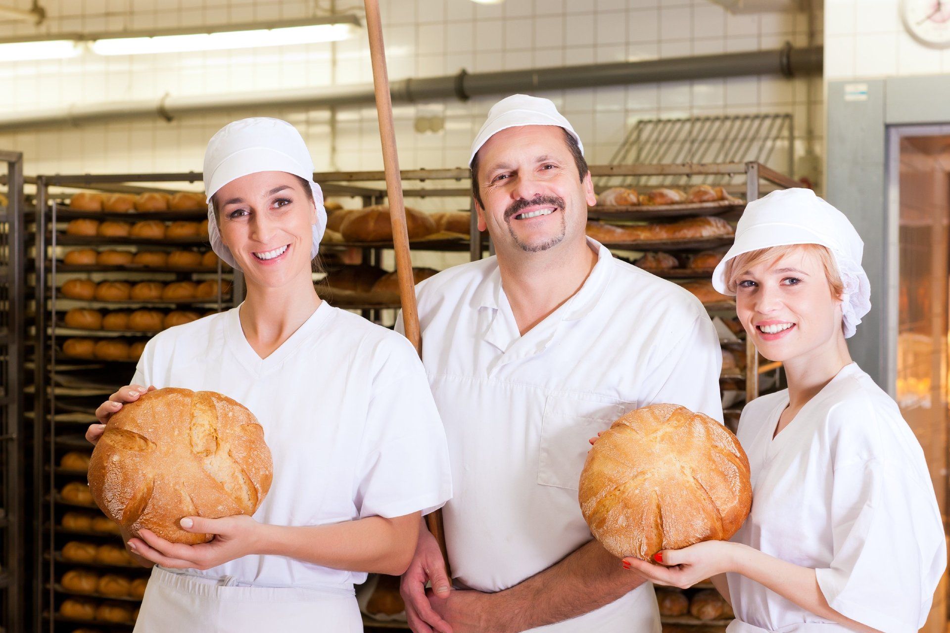 Mitarbeitende einer Bäckerei, die Brot in der Hand halten und in die Kamera lächeln