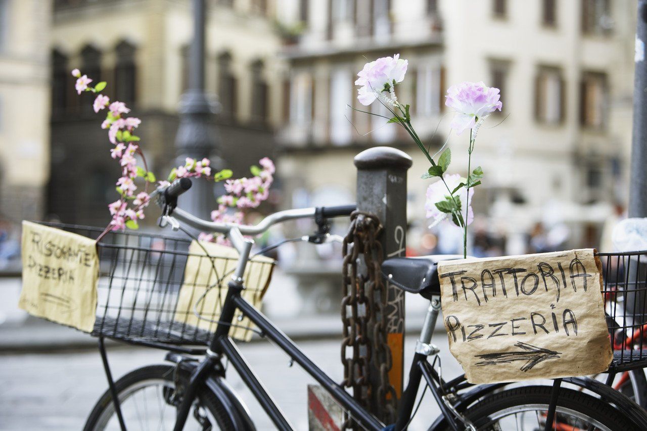 A bicycle chained to a post, with signs in Italian hanging from it.