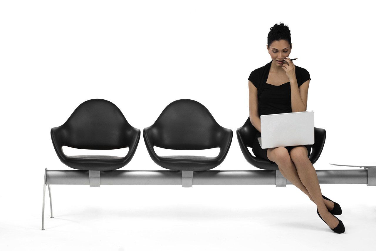 Elegant lady in black, sitting on a black bank of chairs and  studying on her laptop