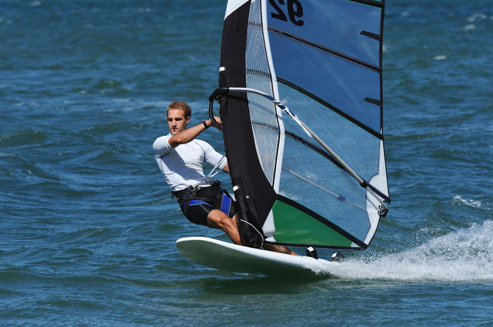 Male windsurfer, leaning on his surf board in a strong breeze.