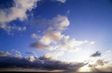 Blauer Himmel mit weißen Wolken, dazwischen durchscheinende Sonnenstrahlen.