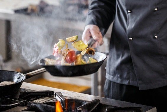 Mann beim Livekochen, der eine Pfanne über dem Feuer schwenkt.