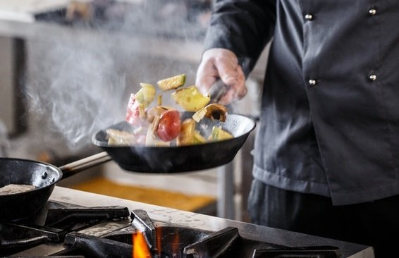 Mann beim Livekochen, der eine Pfanne über dem Feuer schwenkt.