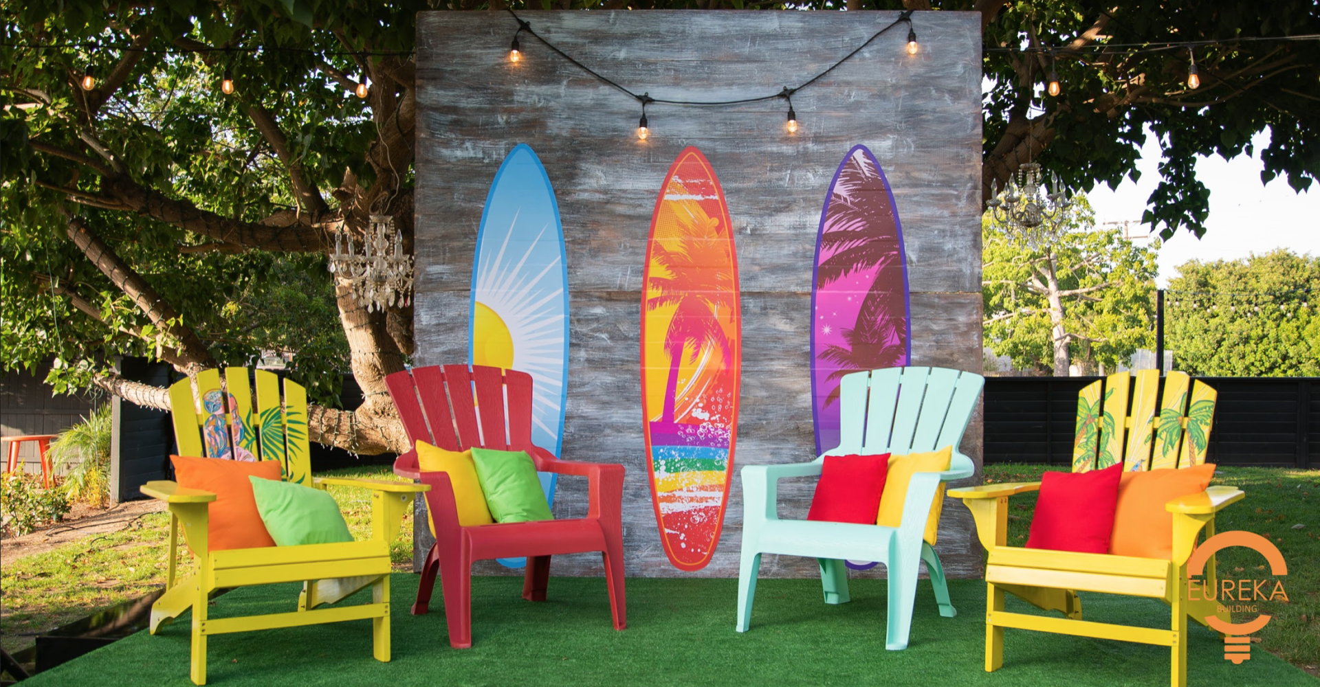 A beach-bash home setup. It has 4 wood lawn chairs along with 3 surfboards in the back.