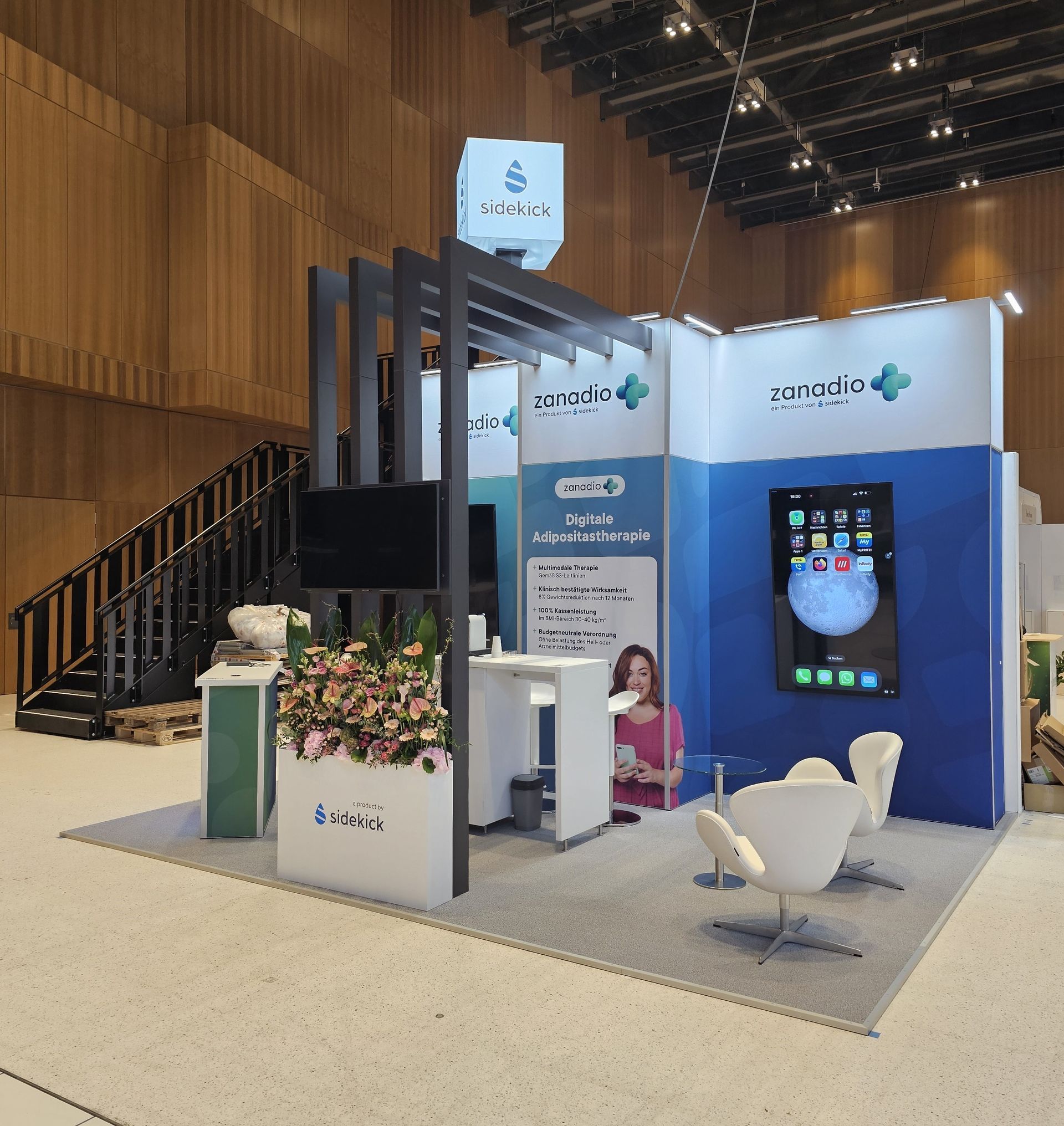 Moderne Messestandgestaltung von Seismo Factory auf einer Messe, präsentiert mit einem auffälligen roten Banner und interaktiven Displays. Der Stand hebt das Motto 'Good Design is Good Business' hervor und nutzt geometrische Designelemente, um Besucher anzuziehen. Ideal für Unternehmen, die kreative und ansprechende Markenpräsentationen suchen.