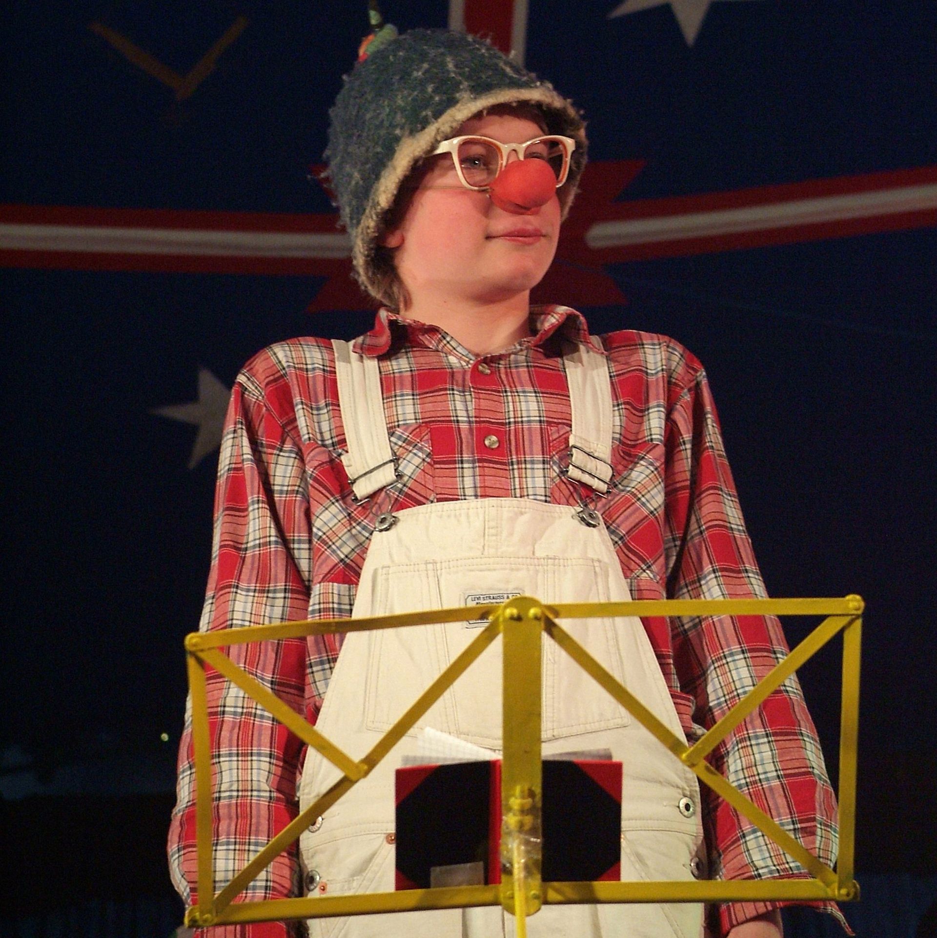 Im Zirkuszelt steht ein als Clown verkleideter Trainierender vor einem leeren Notenhalterung.