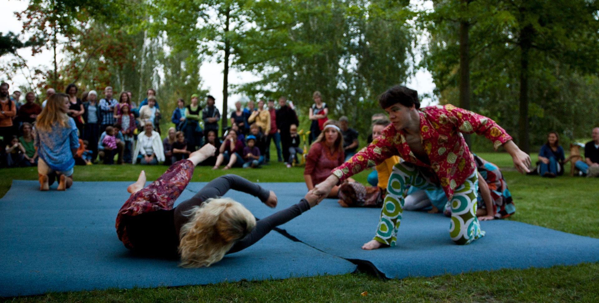 Auf einer Wiese sind 2 Matten ausgelegt. Trainierende zeigen ein Stück. Es gibt Zuschauer.