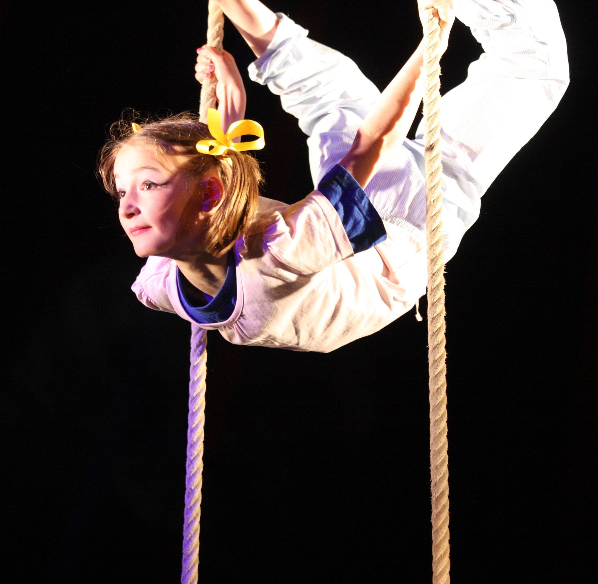 IM Zirkuszelt: eine Trainierende hält sich an Seilen fest mit den Händen und Füßen.