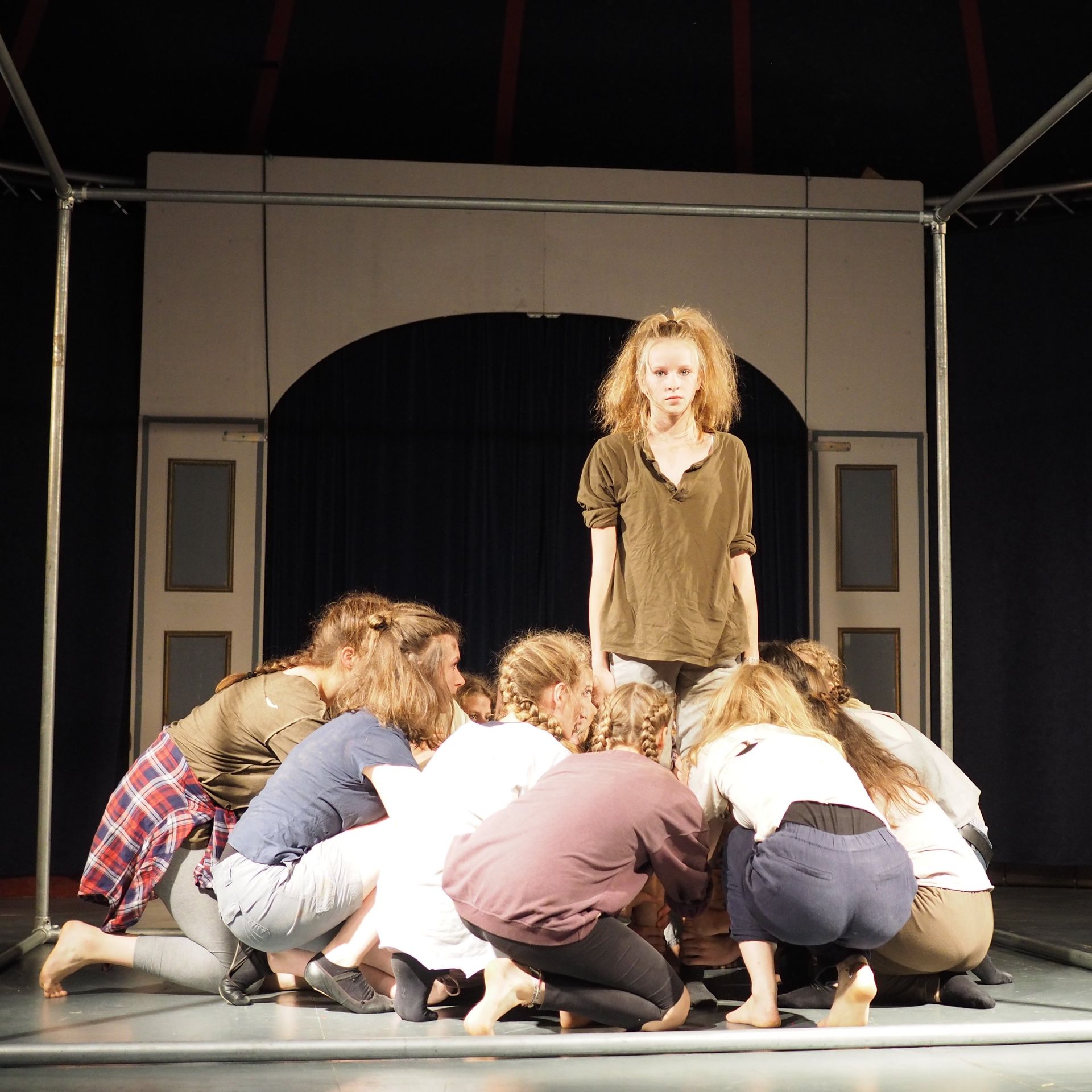 im Zirkuszelt: ein Mädchen steht. Im Vordergrund hocken 6 Mädchen und stecken die Köpfe zusammen.