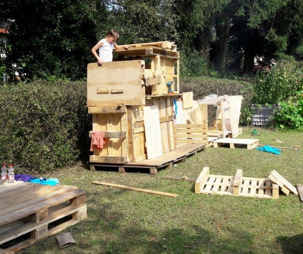 Draußen: Kinder bauen aus Paletten ene Art Haus. Projekt: Kinder bauen ihre Stadt.