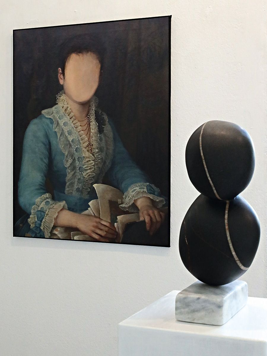 Zwei Kunstwerke in der Ausstellung Faceless: Das ältere Gemälde einer Frau in einem hellblauen Kleid, der das Gesicht mit einer homogenen hautarbenen Fläche übermalt wurde, und eine Steinskulptur des Künstlers Wieland Schöffner. Foto: Dieter Weißenberger