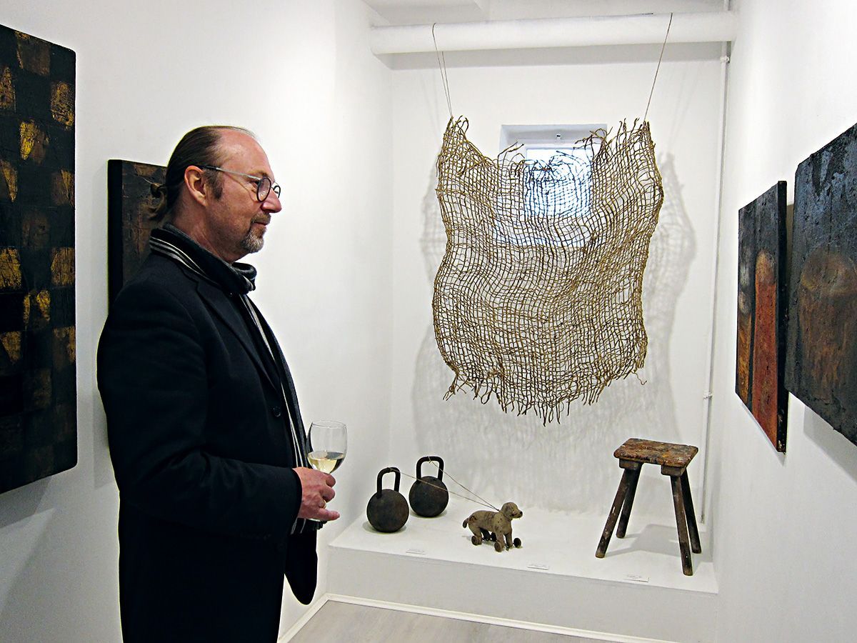 Ein Ausstellungsbesucher mit Weinglas betrachtet konzentriert Werke der Künstlerin Dorothea Panhuyzen. Foto: Dieter Weißenberger