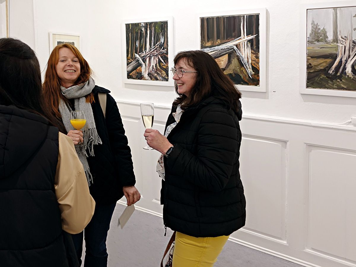 Zwei Künstlerinnen des Vereins mit Sektgläsern im lebhaften Gespräch mit einerAusstellungsbesucherin. Im Hinergrund Werke des Künstlers Albert Reichenbach. Foto: Dieter Weißenberger