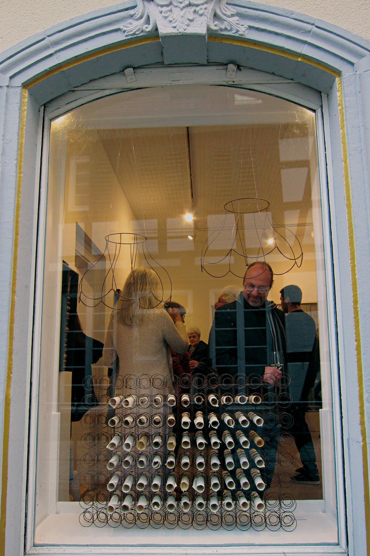Blick durch ein Galeriefenster in einen Ausstellungsraum mit vielen Menschen während einer Vernissage. Foto: Dieter Weißenberger