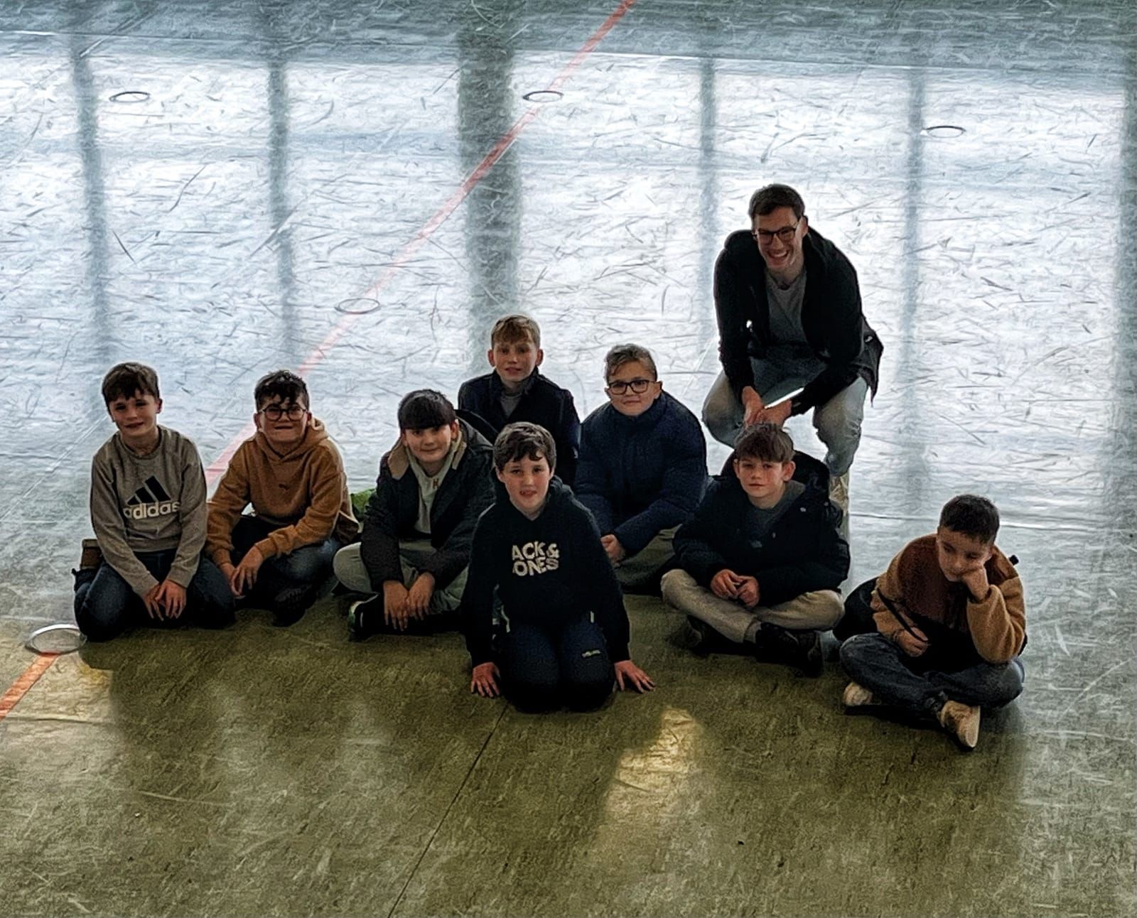 Lehrer und Schüler sitzen auf dem Boden einer Turnhalle