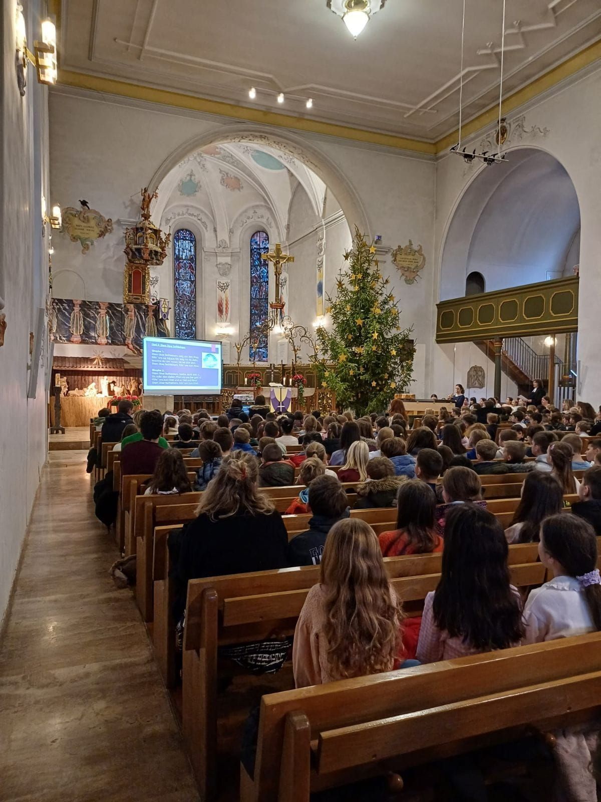 Blick auf Kinder und Lehrkräfte, die auf den Kirchenbänken sitzen.