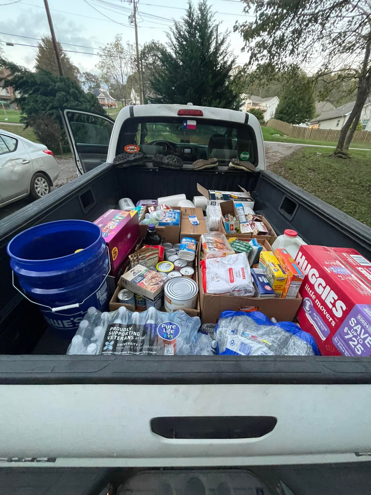 a view of a pick up truck bed filled with staples like bottled water, diapers, and food for hurricane victims