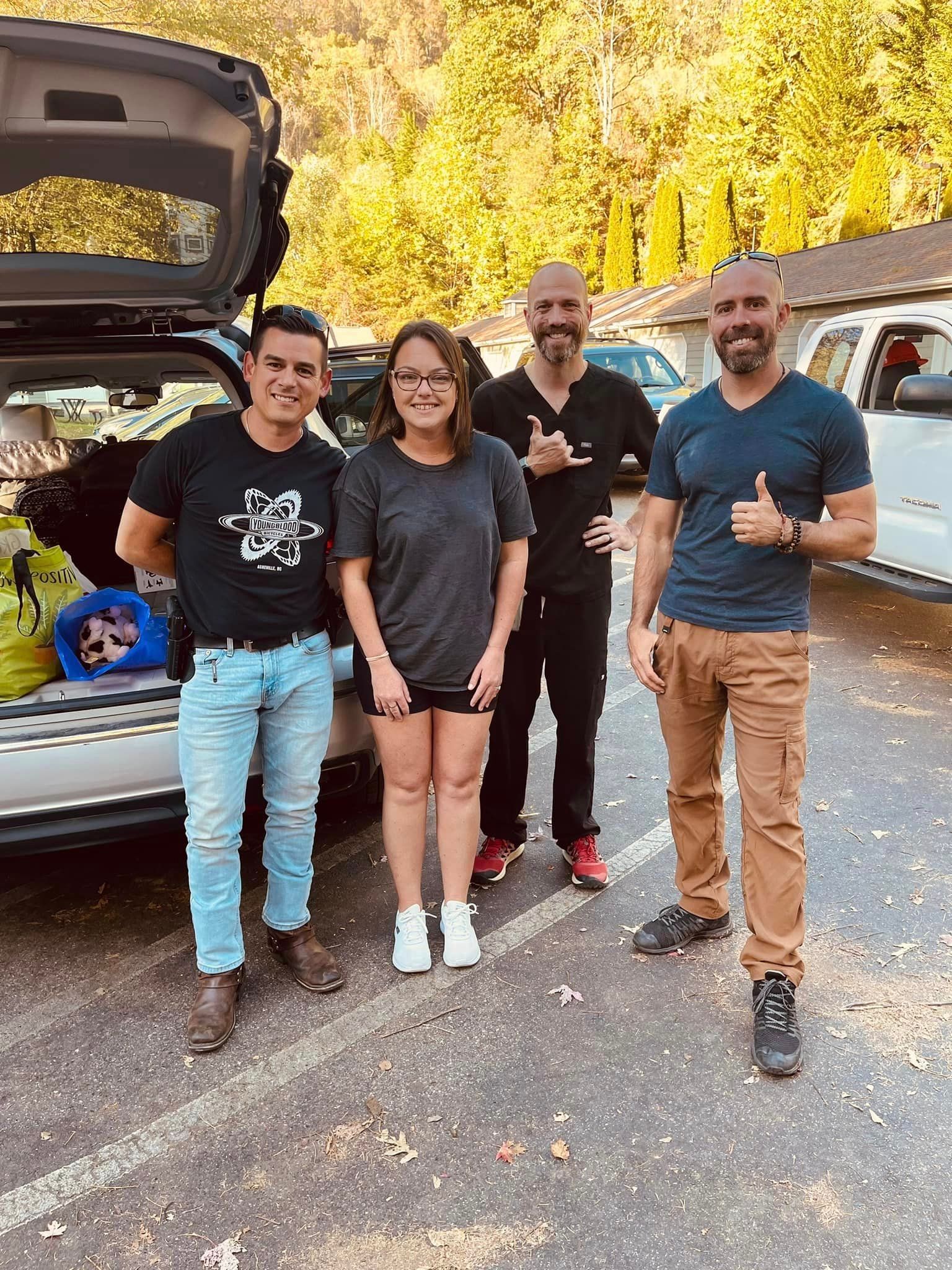 A small group of people stand behind a car with a open back door showing collected supplies for hurricane survivors