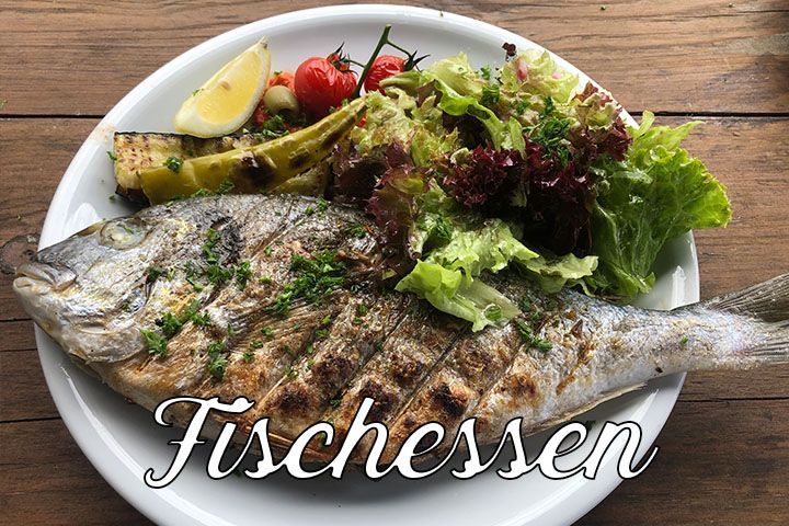 Ein gegrillter Fisch liegt auf einem Teller mit Salat, Gemüse und einer Zitronenspalte. Auf dem Bild steht das Wort „Fischessen“.