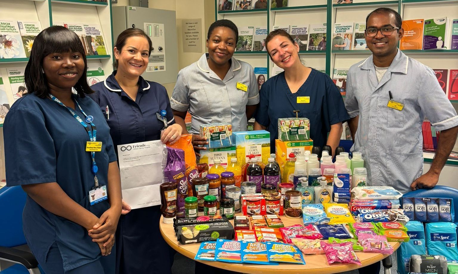 Five nurses in various uniforms standing behind a table of groceries that are part of the Celia Blakey foodbank initiative