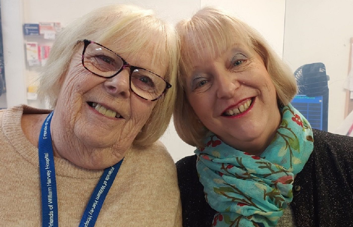 Two smiling women one with glasses, one with a colourful green scarf.