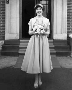 Smiling woman in a mid-length dress holding flowers outside.