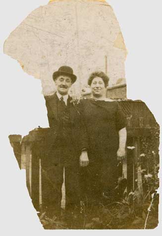 Bride and groom posing outside a doorway, bride in
lace gown holding a bouquet, colour photo.