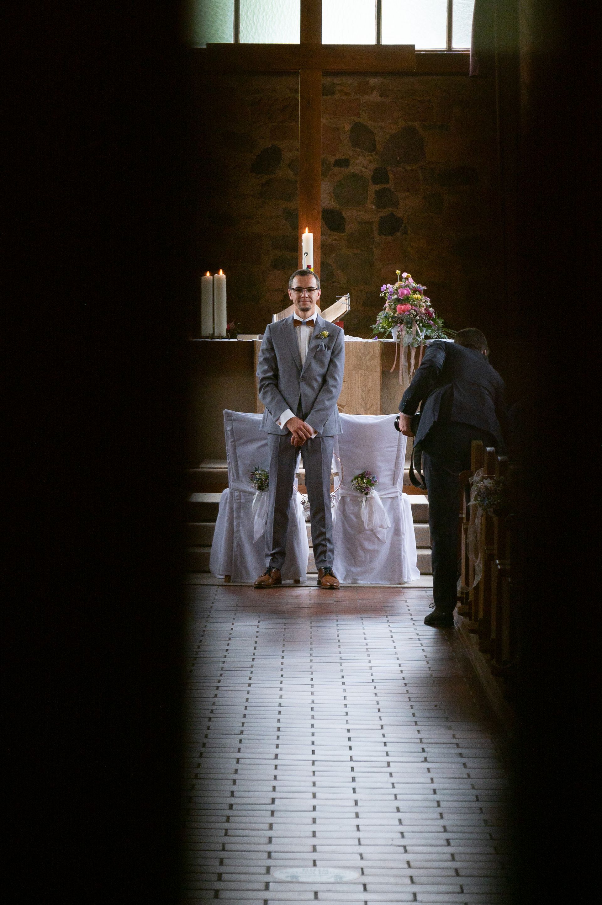 Blick durch die Kirchentür auf den am Altar wartenden Bräutigam