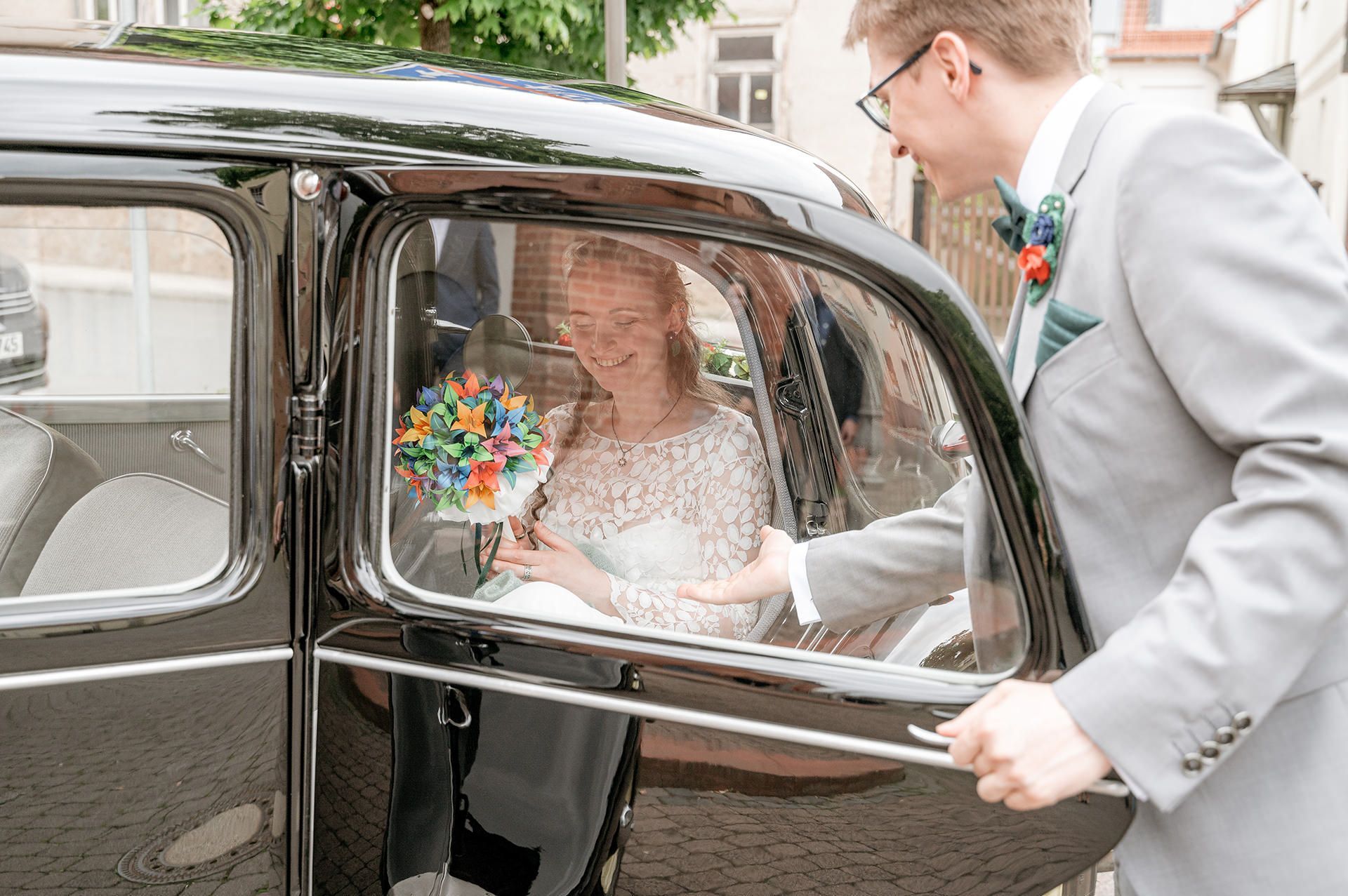 Ein Bräutigam hilft seiner Braut aus einem Vintage-Auto, während sie sich auf ihre Hochzeit vorbereiten.