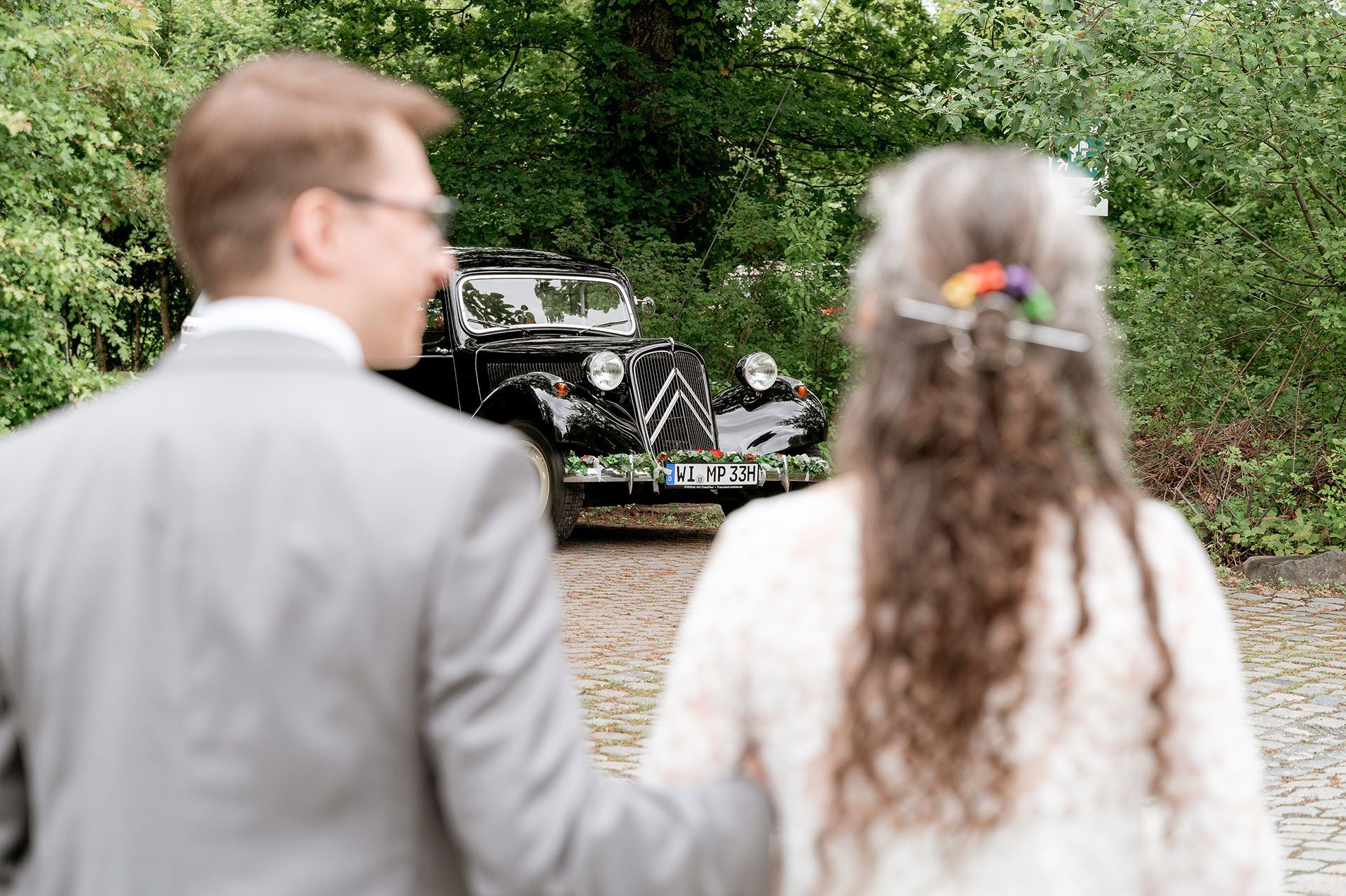 Ein Oldtimer als Brautauto ist zwischen dem Brautpaar hindurch fotografiert
