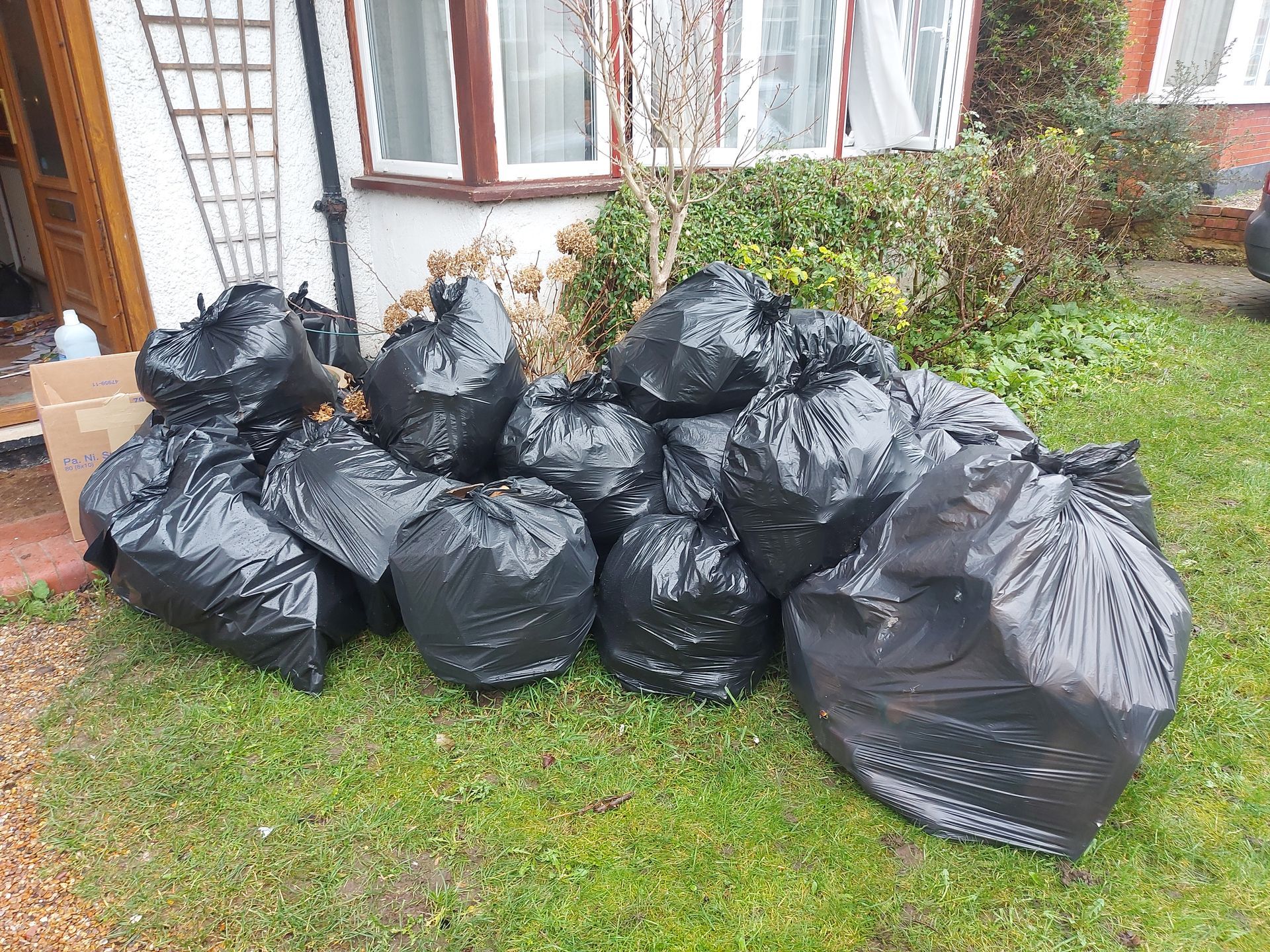 Multiple black bin bags neatly arranged outside a house, awaiting removal. The bags are stacked together, indicating a readiness for clearance and disposal. The image signifies the process of cleaning and organizing, preparing to remove waste and maintain cleanliness around the property