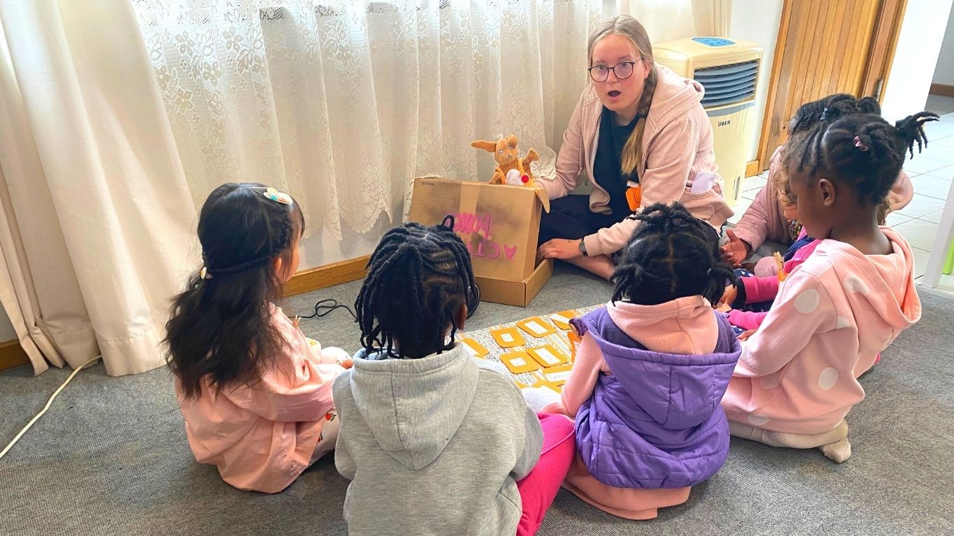 A German volunteer with a rabbit hand puppet teachers a group of children.