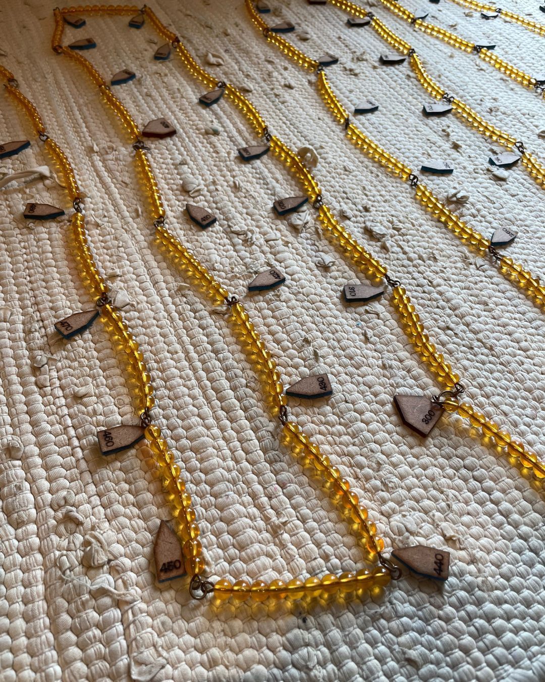 A golden Montessori 1000 bead chain is laid out on a beige mat with wooden arrows to count the multiples of 10.
